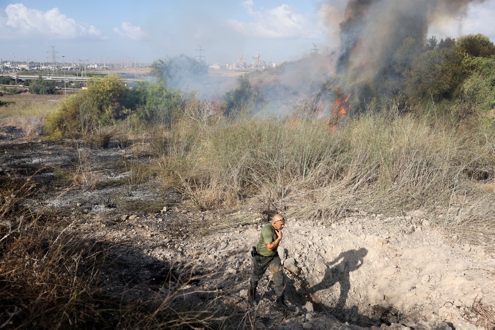 Policial israelense caminha perto de cratera formada após ataque dos houthis — Foto: Ronen Zvulun/Reuters