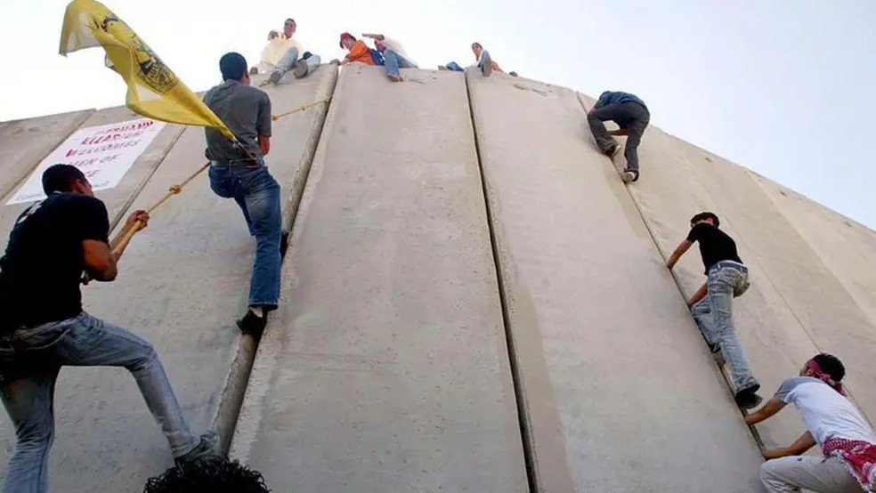 Palestinos escalam o muro que os separa de Israel durante uma marcha pela paz na cidade de Abu Dis, na Cisjordânia — Foto: Foto: Getty Images/BBC
