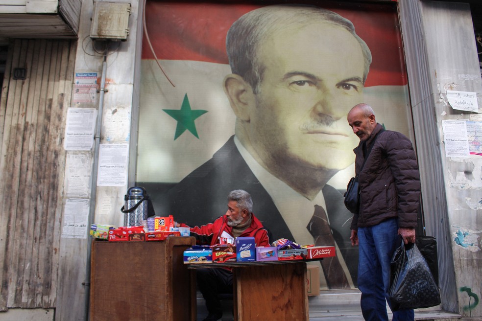 Vendedor em Damasco trabalha em frente a pôster com imagem de Hafez al-Assad, ditador da Síria entre 1970 e 2000, em imagem de 5 de dezembro de 2024 — Foto: Firas Makdesi/Reuters