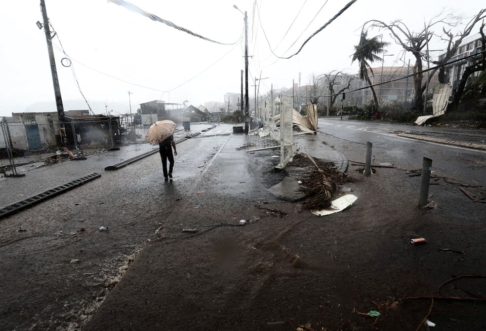 Morador de Mayotte caminha pela capital do arquipélago, Mamoudzou,com guarda-chuva após passagem do ciclone Chido — Foto: Yves Herman/Reuters