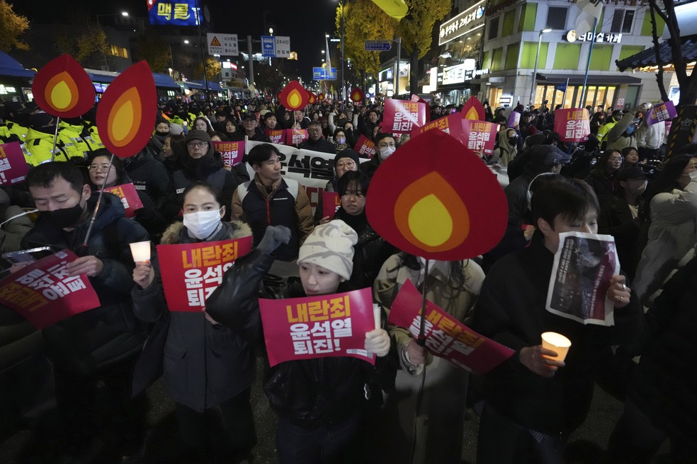 Manifestantes com cartazes escritos "Yoon Suk Yeol, renuncie por traição" marcham em direção ao palácio presidencial em Seul pedindo a renúncia do presidência da Coreia do Sul em 4 de dezembro de 2024. — Foto: AP Photo/Lee Jin-man