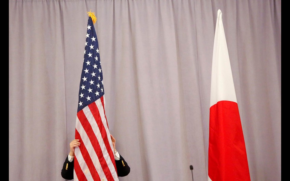 Um funcionário ajeita a bandeira dos EUA ao lado da bandeira japonesa pouco antes de entrevista coletiva do presidente eleito Donald Trump com o primeiro-ministro do Japão, Shinzo Abe, após reunião em Manhattan, Nova York — Foto: Andrew Kelly/Reuters