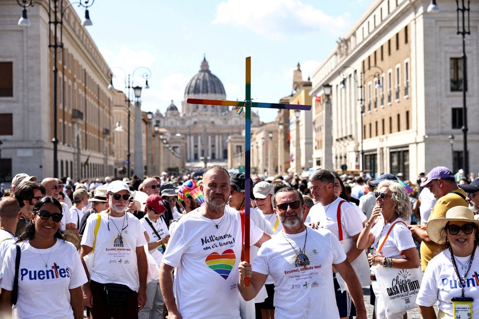 Grupo de fiéis católicos segura cruz com cores da bandeira LBTQIA+ diante da Basílica de São Pedro, no Vaticano, em 6 de setembro de 2025. — Foto: Matteo Minnella/ Reuters