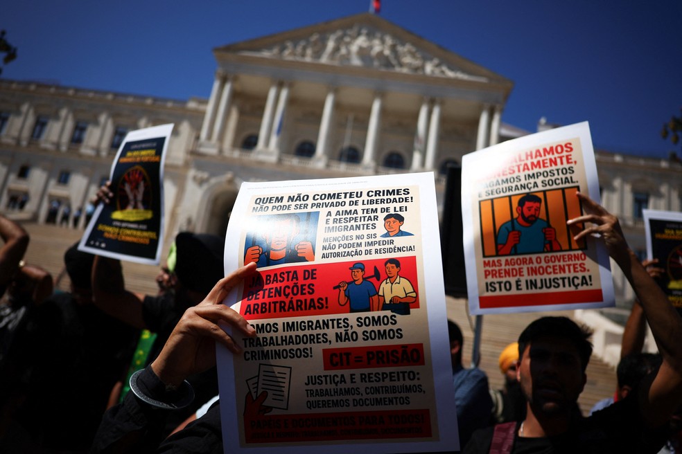 Imigrantes seguram cartazes durante protesto por direitos e autorizações de residência em frente ao Parlamento português, em Lisboa, Portugal, em 17 de setembro de 2025. — Foto: REUTERS/Pedro Nunes