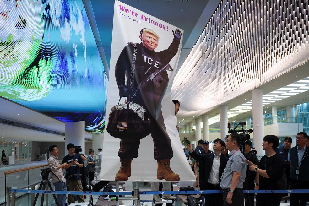 Cartaz com críticas ao governo Trump é erguido em recepção a sul-coreanos presos pelos EUA e repatriados pelo governo da Coreia do Sul em 12 de setembro de 2025. — Foto: REUTERS/Kim Hong-ji