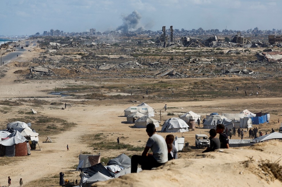 Palestinos olham para fumaça ao longe de ataque de Israel na Faixa de Gaza em 5 de outubro de 2025. — Foto: REUTERS/Mahmoud Issa