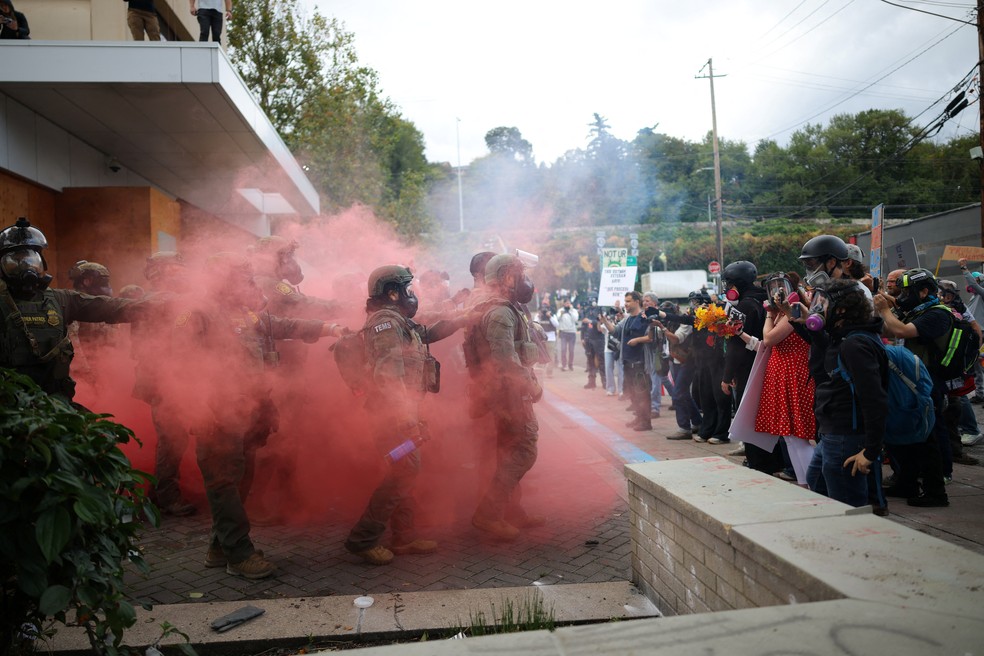 Manifestantes usam seus telefones enquanto policiais estão em meio à fumaça em frente à sede do Departamento de Imigração e Alfândega dos EUA (ICE) em Portland, Oregon (EUA) — Foto: REUTERS/Carlos Barria