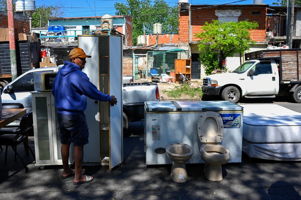 Um homem mostra um guarda-roupa de segunda mão à venda em um mercado de rua em Villa Fiorito, nos arredores de Buenos Aires. — Foto: LUIS ROBAYO/AFP