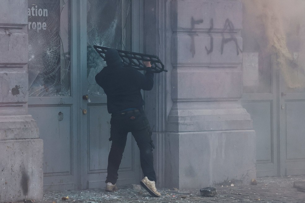 Manifestante quebra janela em prédio em Bruxelas durante protesto de agricultores contra o acordo entre União Europeia e Mercosul, em 18 de dezembro de 2025 — Foto: REUTERS/Yves Herman