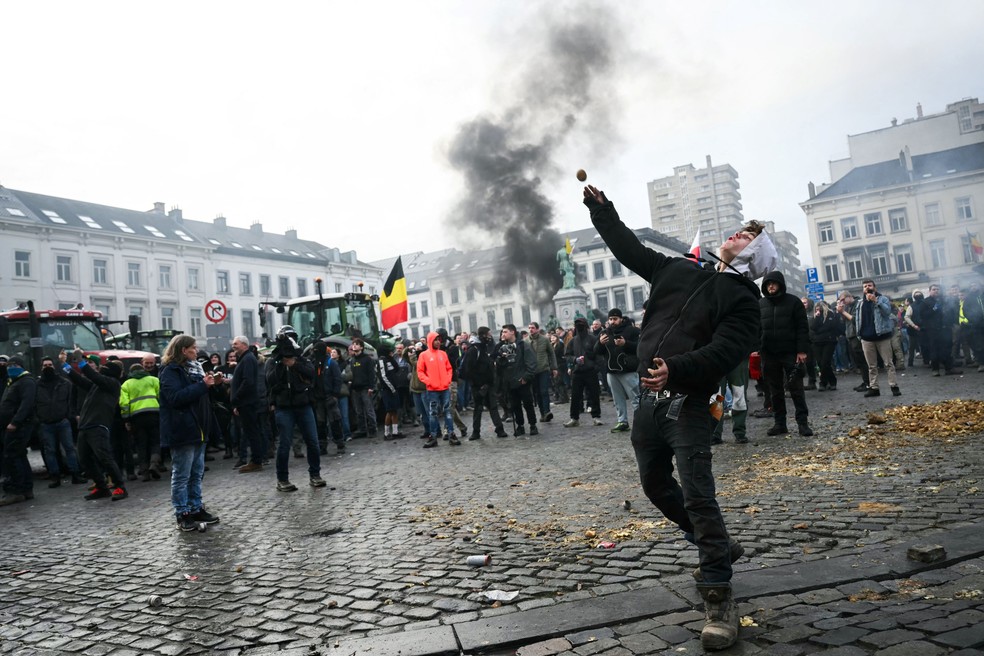 Manifestante atira batata em direção à polícia perto do prédio do Parlamento Europeu em Bruxelas; agricultores protestam protesto contra o acordo entre União Europeia e Mercosul — Foto: NICOLAS TUCAT / AFP