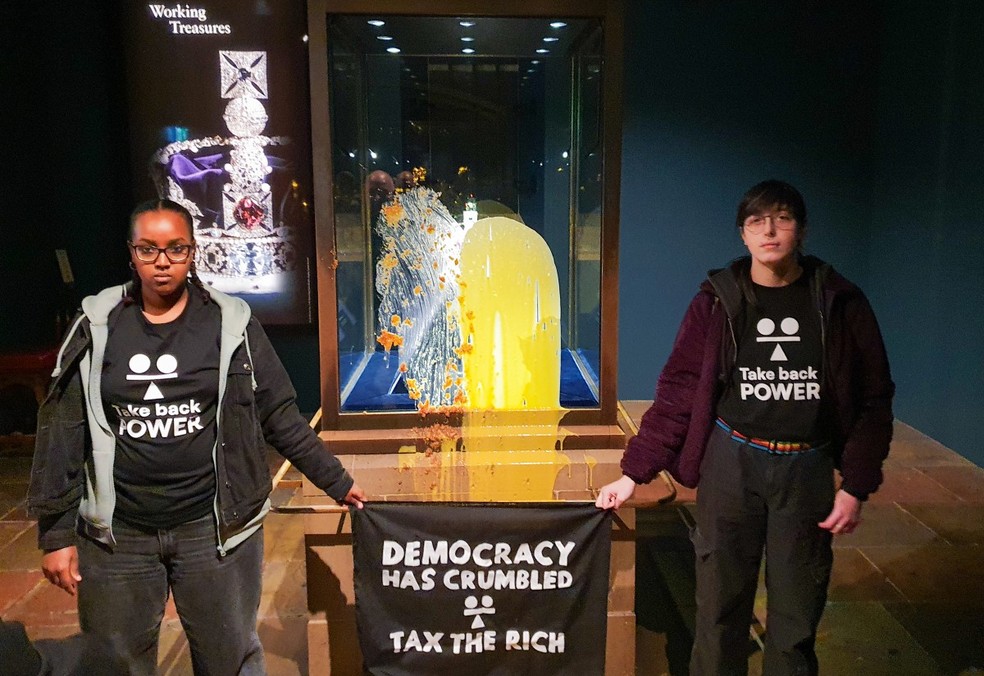 Grupo Take Back Power segura faixa com os dizeres "A democracia desmoronou - Taxem os ricos" — Foto: TAKE BACK POWER / AFP