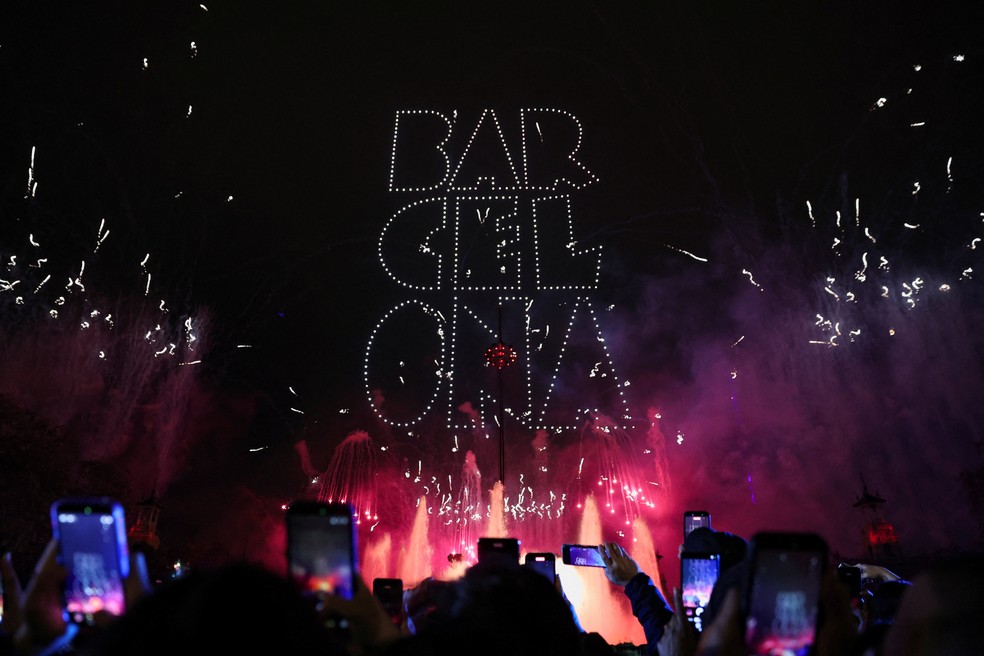 Drones formam a palavra "Barcelona" no céu noturno enquanto fogos de artifício iluminam a cidade durante as comemorações de Ano Novo na cidade da Espanha — Foto: REUTERS/Bruna Casas
