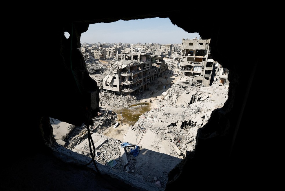 Palestinos caminham entre os escombros de prédios destruídos, em meio a um cessar-fogo entre Israel e o Hamas, em Gaza. — Foto: Reuters