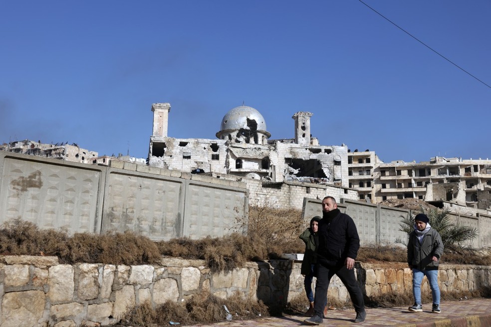 Moradores do bairro Sheikh Maqsoud caminham entre prédios danificados em Aleppo — Foto: Bakr Alkasem/AFP