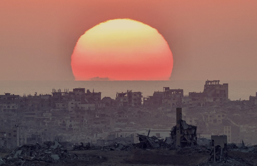 28 de julho - O sol se põe sobre o cenário de destruição após inúmeros bombardeios no norte de Gaza, visto do lado israelense da fronteira — Foto: Amir Cohen/Reuters