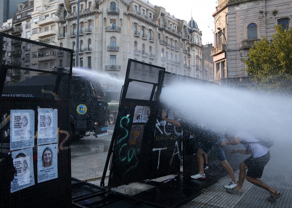 Manifestantes empurram uma cerca enquanto um canhão de água tenta dispersá-los durante um protesto em frente ao prédio do Congresso em Buenos Aires, durante discussões da reforma trabalhista no país — Foto: TOMAS CUESTA / AFP