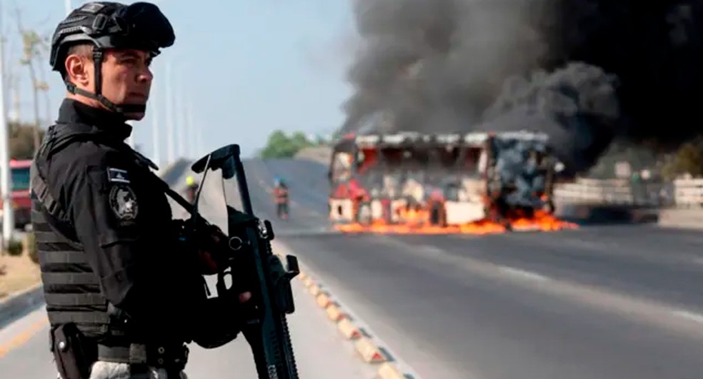 Agente de segurança segura metralhadora em frente a ônibus em chama em Zapopan, no estado de Jalisco, no México, após morte de traficante — Foto: Ulises Ruiz/AFP via Getty Images