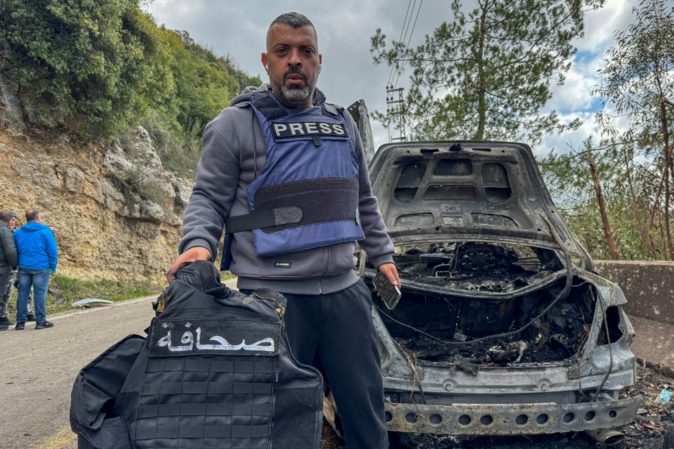 O jornalista Jamal Al-Gharabi, da Al Mayadeen, segura um colete de imprensa ao lado de um carro destruído por um ataque israelense matou três de seus colegas: Fatima Ftouni (repórter da Al Mayadeen) e Mohammed Ftouni (cinegrafista), e Ali Shaib (repórter da Al Manar) — Foto: Ali Hankir/Reuters