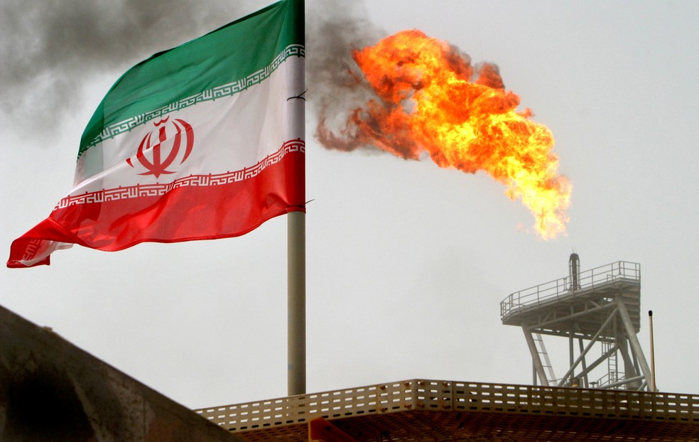 Uma tocha de gás em uma plataforma de produção de petróleo nos campos de petróleo de Soroush é vista ao lado de uma bandeira iraniana no Golfo Pérsico, no Irã — Foto: Raheb Homavandi/File Photo/Reuters