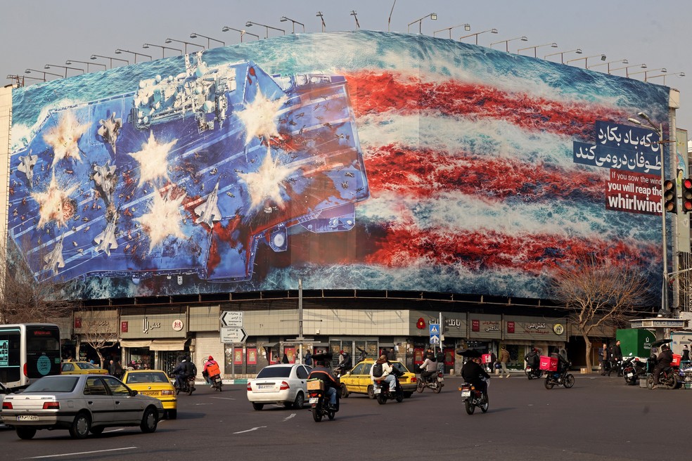 Carros passam por outdoor que mostra porta-aviões americano bombardeado no centro de Teerã, capital do Irã — Foto: ATTA KENARE / AFP