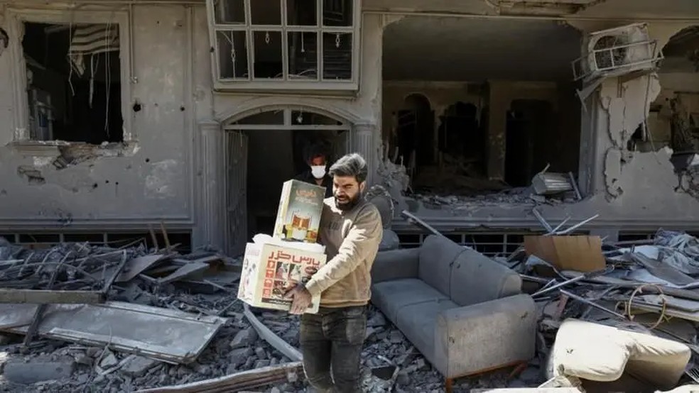 Homem carrega caixas de uma casa danificada por ataques em Teerã, capital do Irã, na segunda-feira (30) — Foto: Reuters
